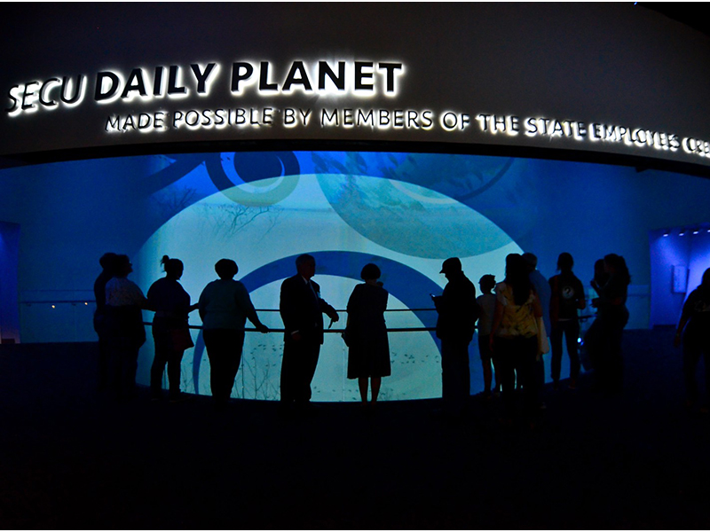 View of the Daily Planet Theater from the 2nd Floor. Visitors are silhouetted in front of a lit screen