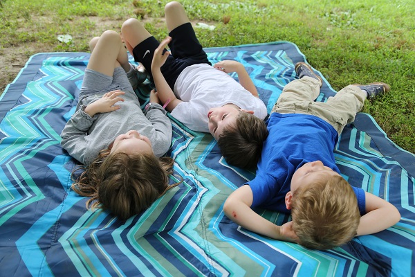 Children lounge on a blanket under a summer sky.