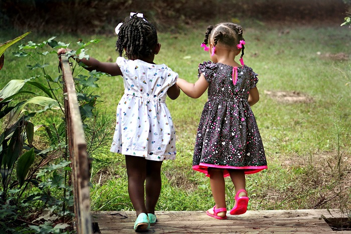 Two little girls in braids hold hands and go for a lovely walk outdoors.