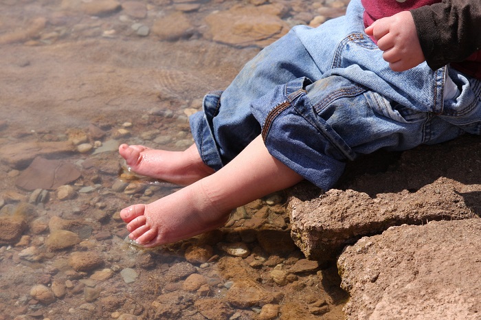 A baby's feet splash in a clear stream.