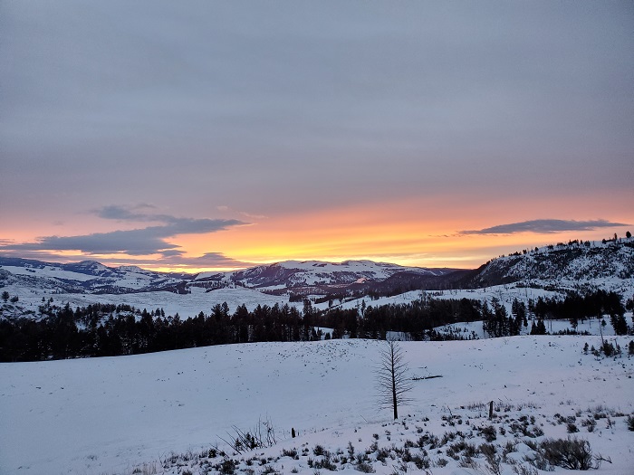 A brilliant sunset dips behind a shadowy, snowy mountain.