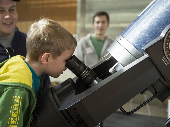 Child curiously peers into a large telescope.