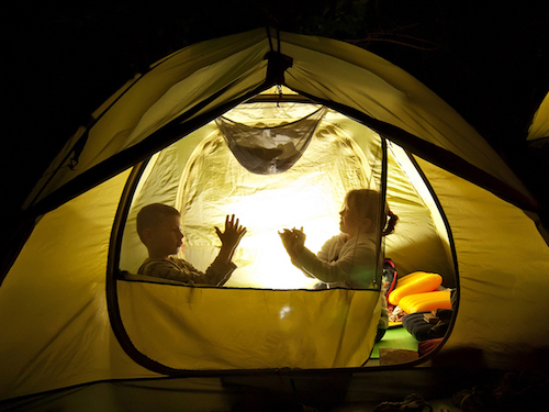 Children create shadow puppets in a tent.