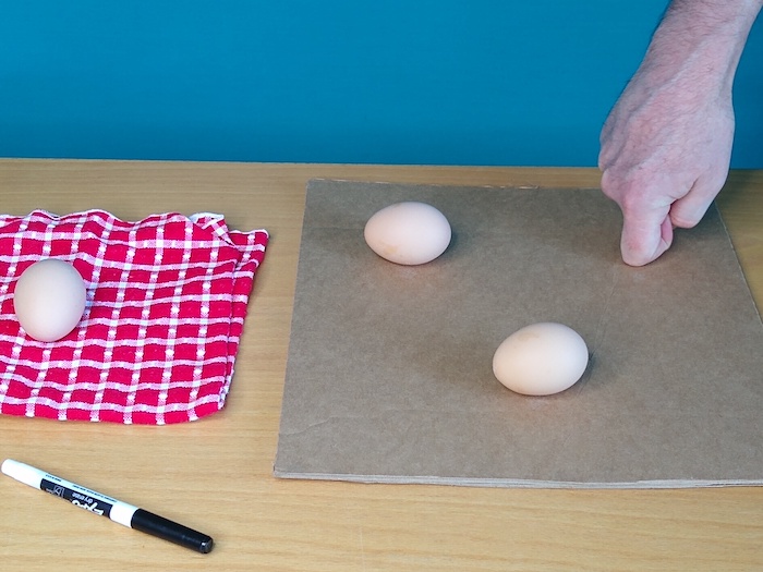 A person uses their knuckle to make an indention in cardboard.