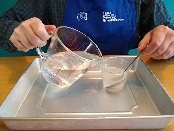 Someone pours water into a smaller cup of salty water.