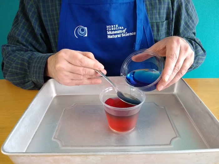 The person slowly drips the blue water into the spoon.
