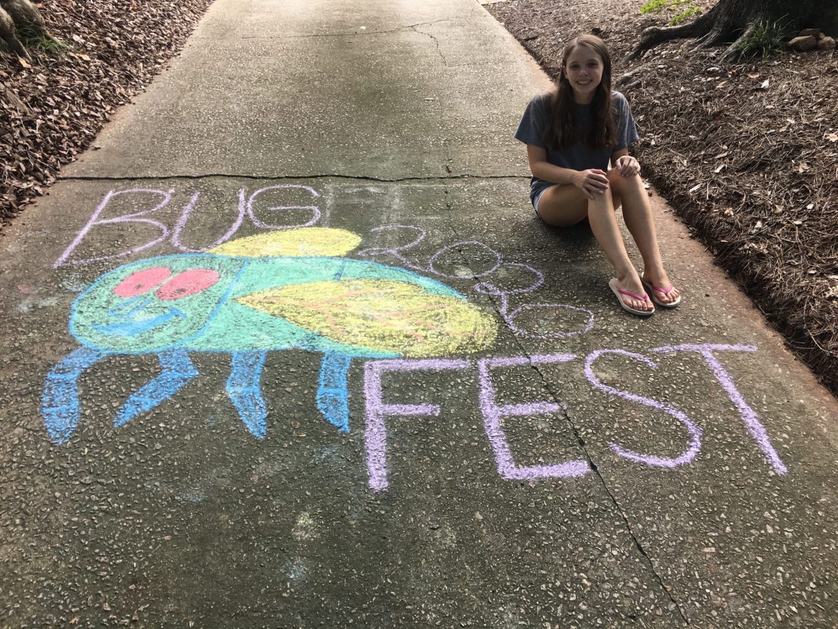 A girl sitting next to a chalk rainbow bug and bugfest