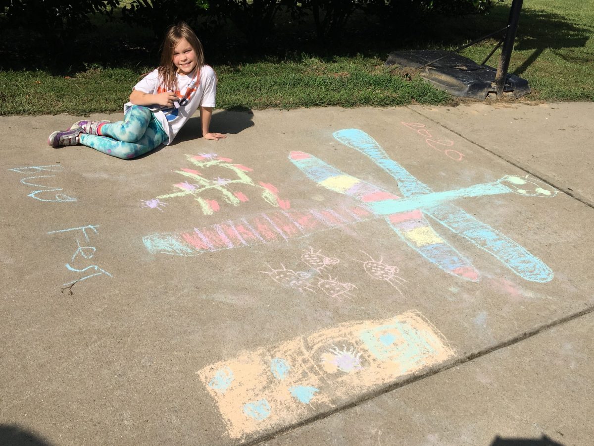 a little girl with a big chalk dragonfly