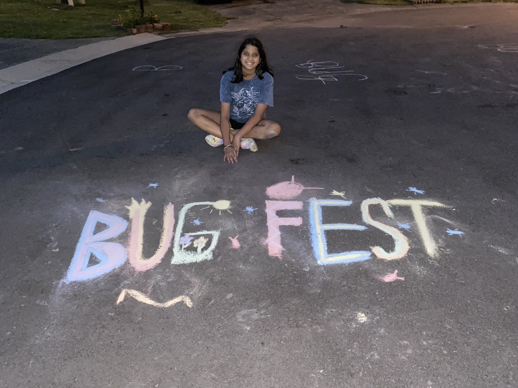 A girl sitting cross-legged by a BugFest chalk drawing