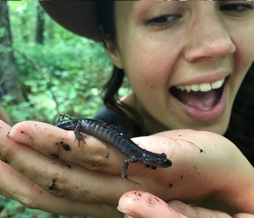 A smiling woman holding a black salamander