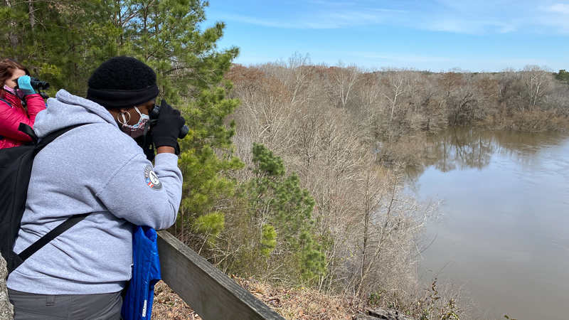 Americorps Member and Teacher Education Specialist Taylor Prichard scans the Neuse River for birds.