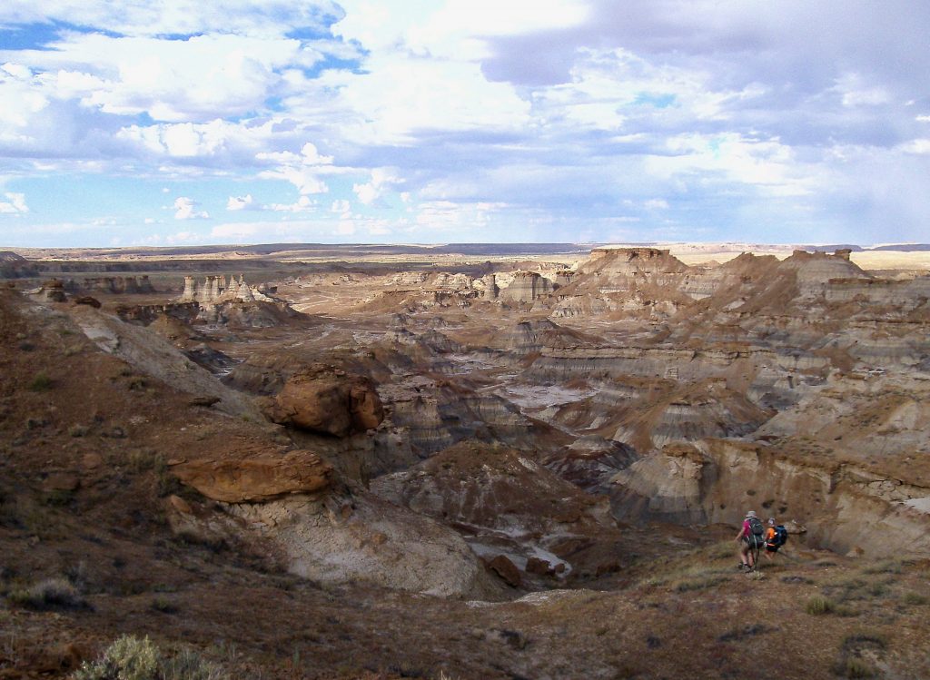 Landscape photo of desert rocky cliff formations with two people in backpacking gear hiking downhill