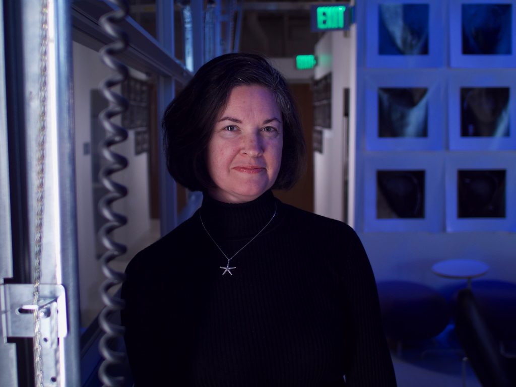 photo of a woman with dark hair and dark-colored turtleneck shirt in a laboratory