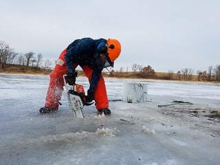 Dr. Ami Thompson clearing a hole for ice fishing with a chainsaw.