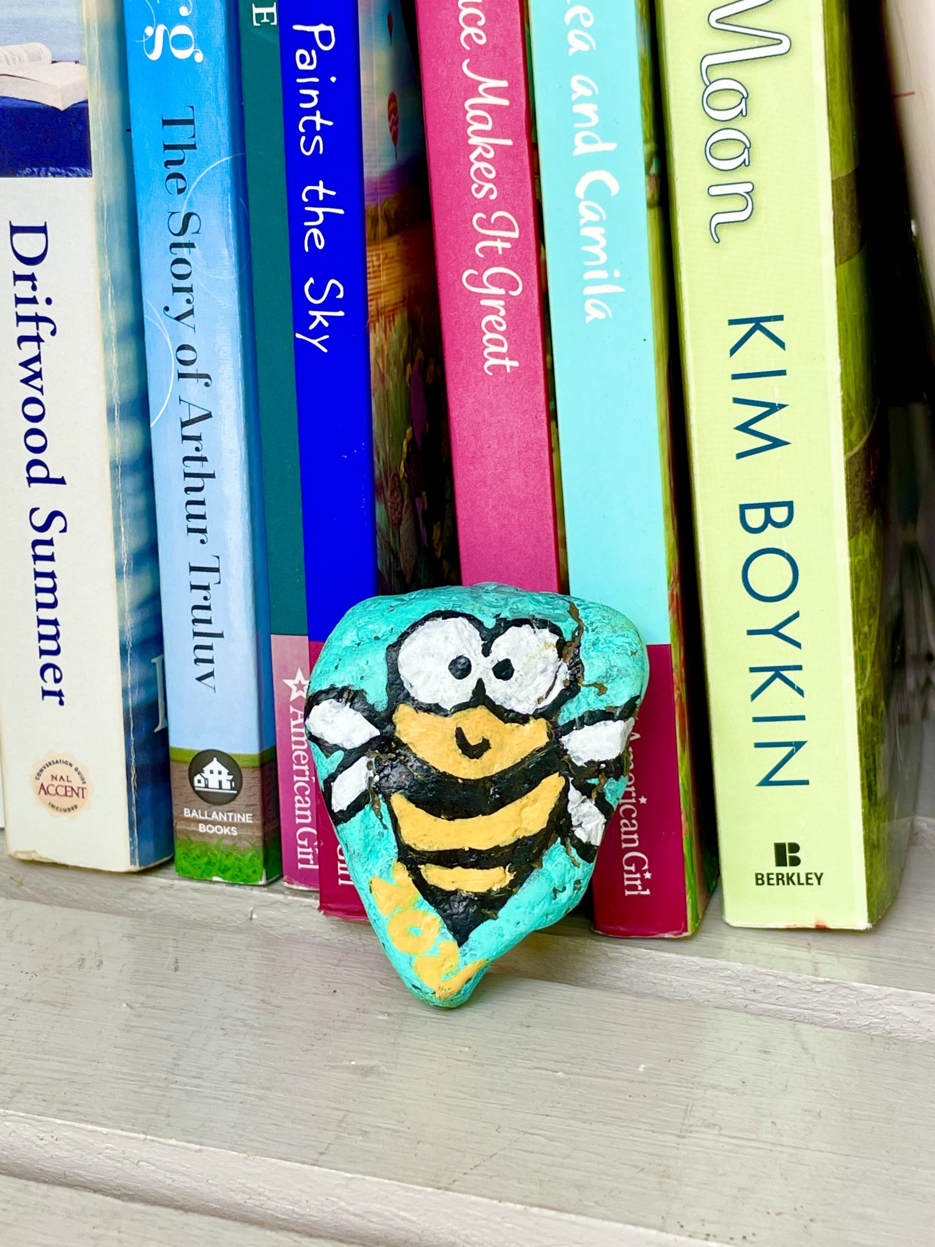 A bee painted on a rock by books