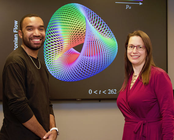 Two people standing on either side of a multicolored physics graphic depicting complex systems