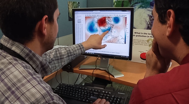 Man pointing at computer screen with weather map while a second man looks on.