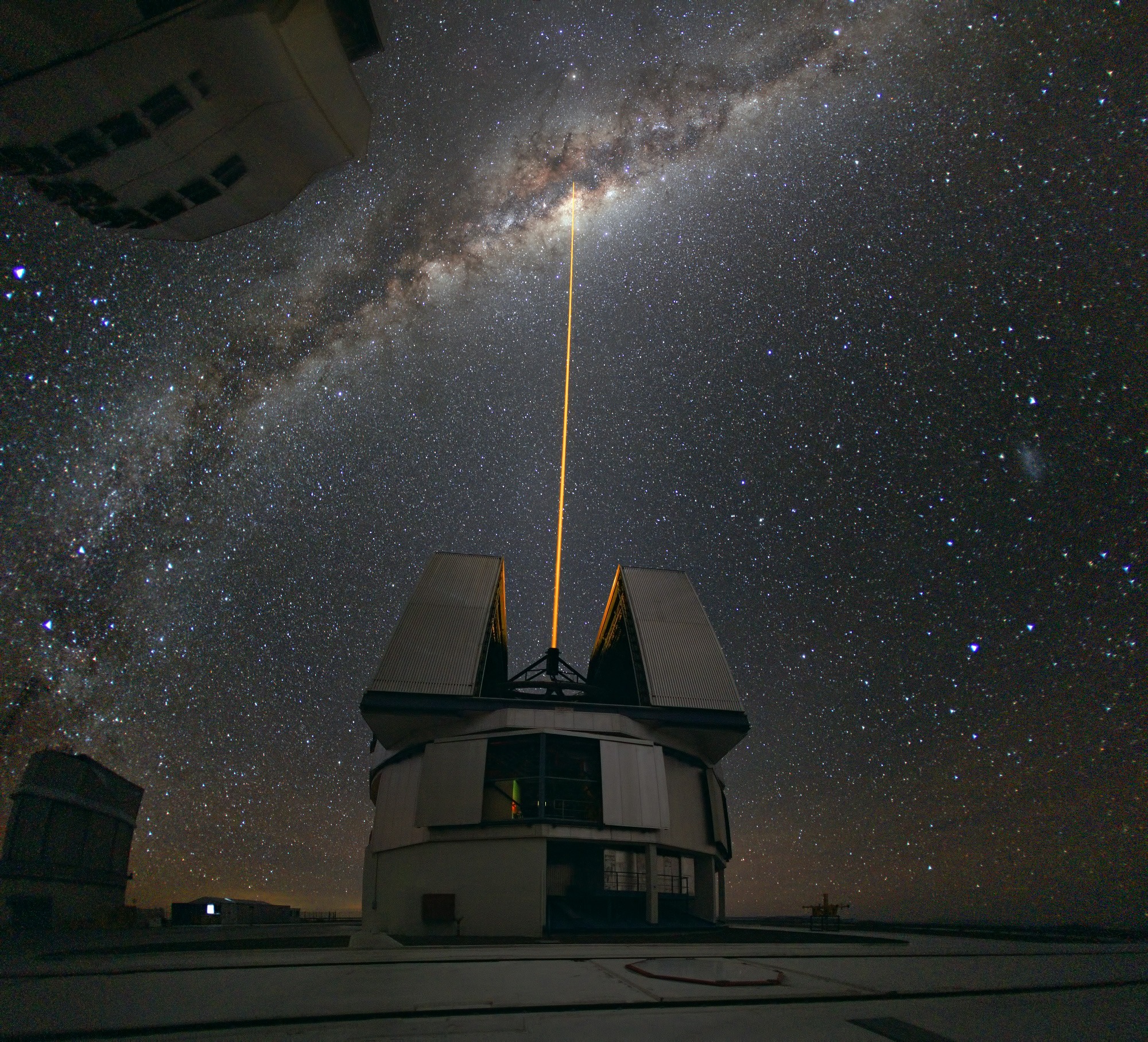 A laser beam towards the Milky Way's center emitted from an observatory with the Milky Way galaxy in the background.