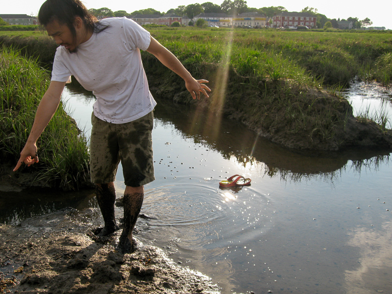 Man points to where he lost his shoe in the mud of an estuary.