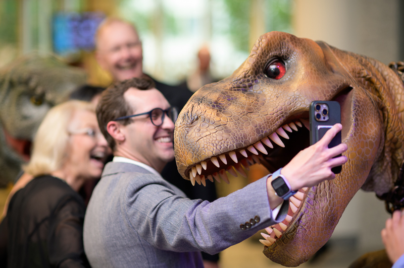Guest at a Museum event poses for selfie with carnivorous dinosaur puppet.