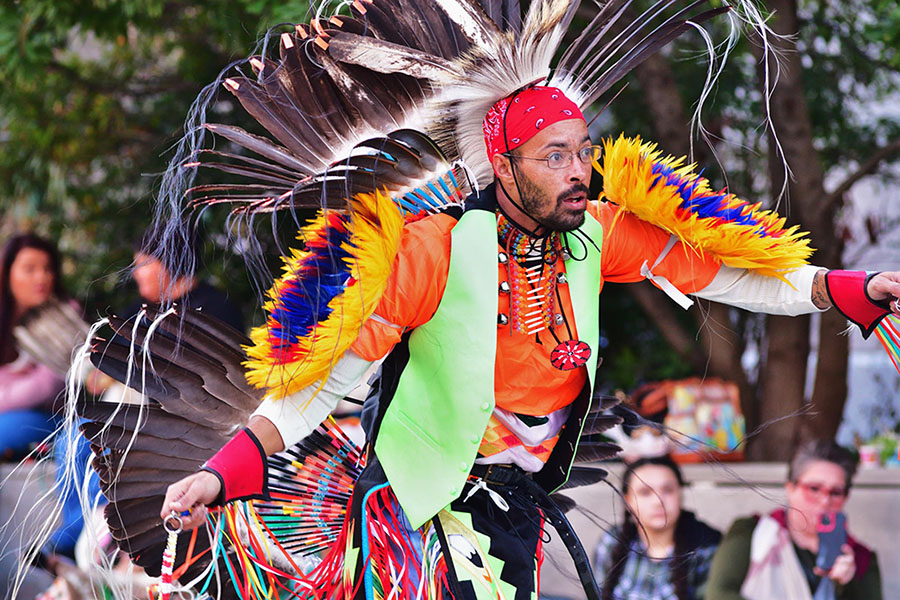 A man in brightly-colored attire with feather trim demonstrates a traditional dance at the American Indian Heritage Celebration.