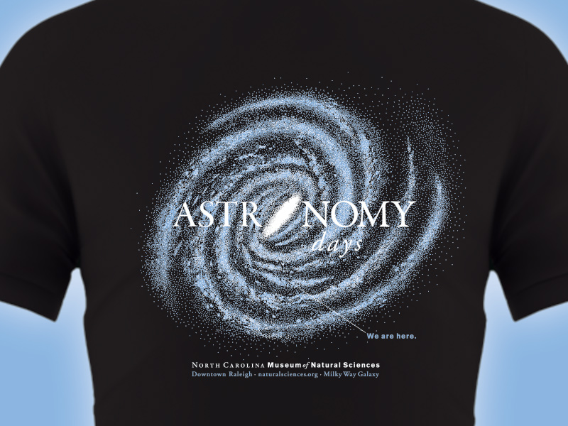 Astronomy Days 2025 T-shirt: image of the Milky Way Galaxy with a "You are here" indicator for Earth on a black T-shirt.