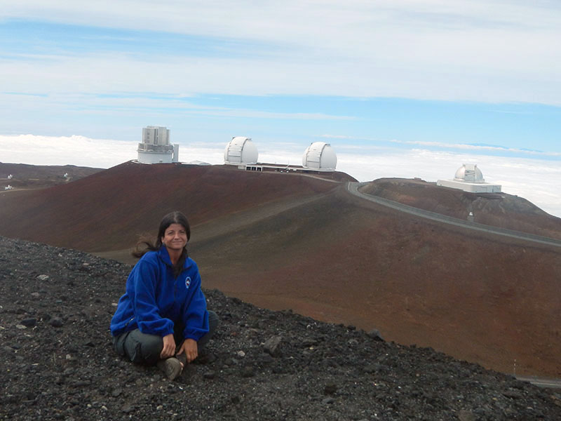 Dr. Rachel Smith sits on a hilltop overlooking observatory in Maunakea, Hawaii