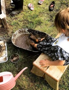 young girl puts feet in bucket filled with mud