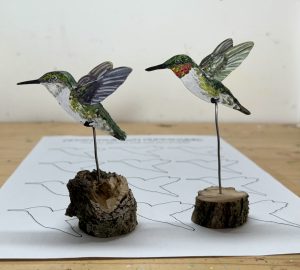 two art pieces of hand painted hummingbirds mounted to a base made of natural wood