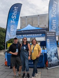 three people stand in front of an information station regarding memberships to the museum