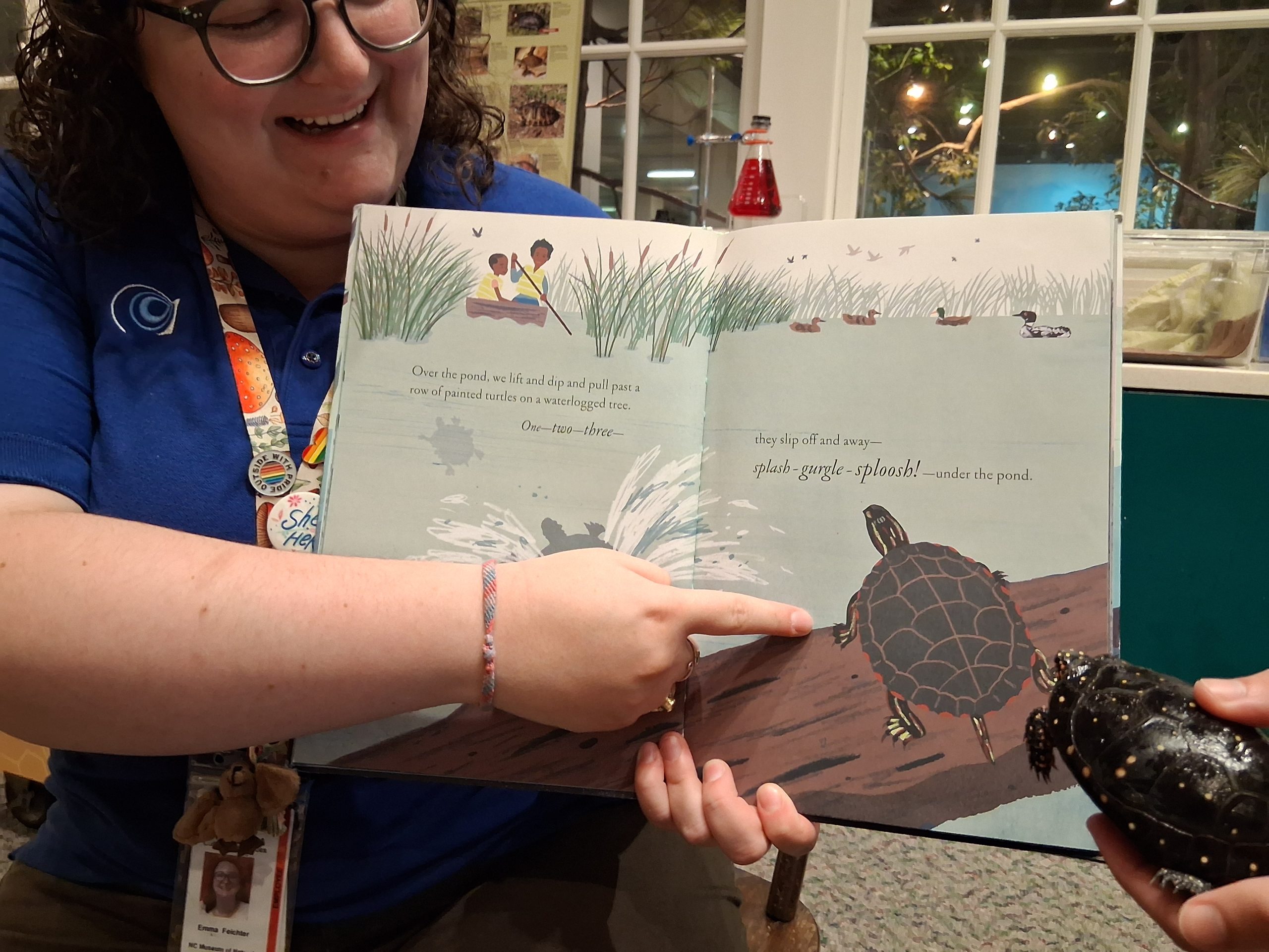 a woman points to an illustration of a turtle on a page in an open book