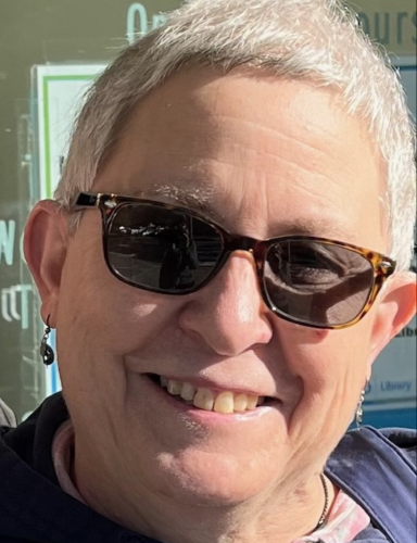 Woman with short gray hair and sunglasses is smiling at the camera. 