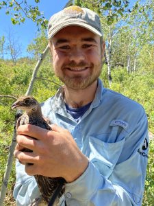 Photo of Will Harrod smiling and holding a bird in a forest
