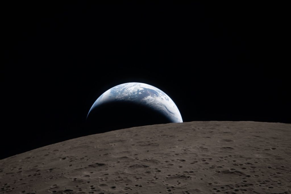 Earthset captured through the Orion spacecraft window at 6:41 p.m. EDT, April 6, 2026, during the Artemis II crew’s flyby of the Moon. A muted blue Earth with bright white clouds sets behind the cratered lunar surface. The dark portion of Earth is experiencing nighttime. On Earth’s day side, swirling clouds are visible over the Australia and Oceania region. In the foreground, Ohm crater has terraced edges and a flat floor interrupted by central peaks. Central peaks form in complex craters when the lunar surface, liquefied on impact, splashes upwards during the crater’s formation.Image Credit: NASA